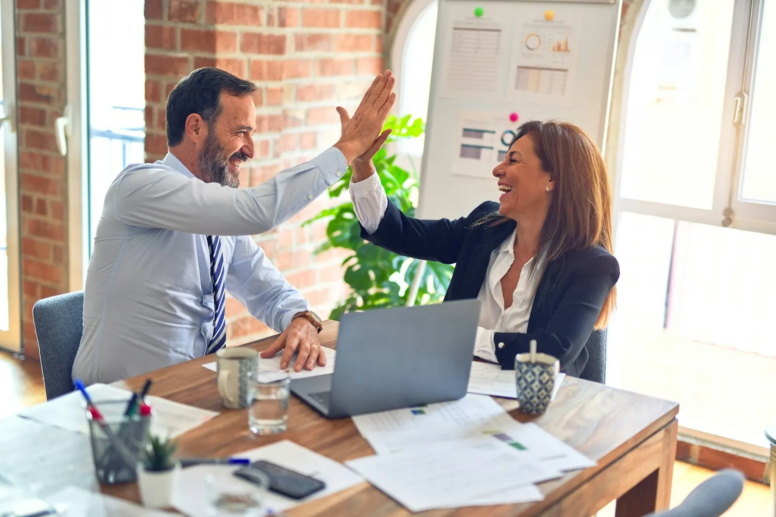 Two colleagues celebrating a win over a laptop
